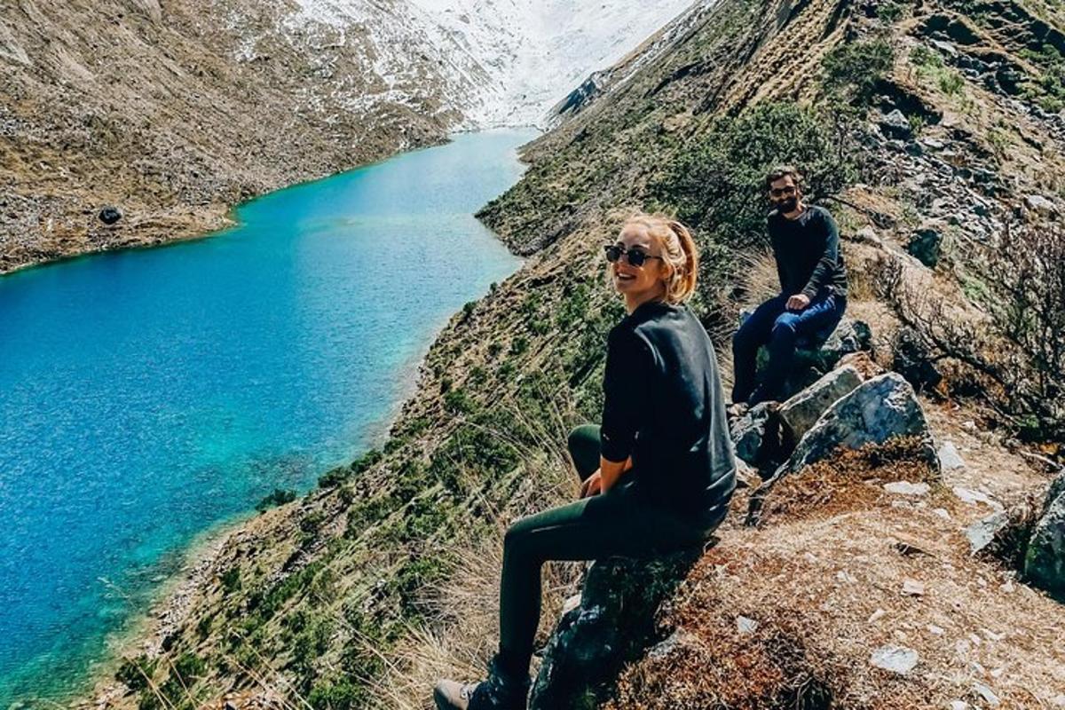two people sitting on a rock near a lake