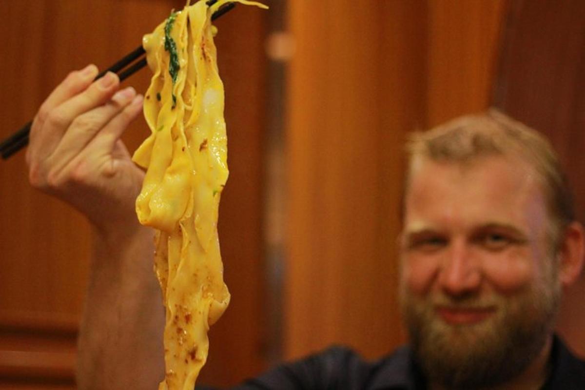 a man holding up a piece of food on a chopstick