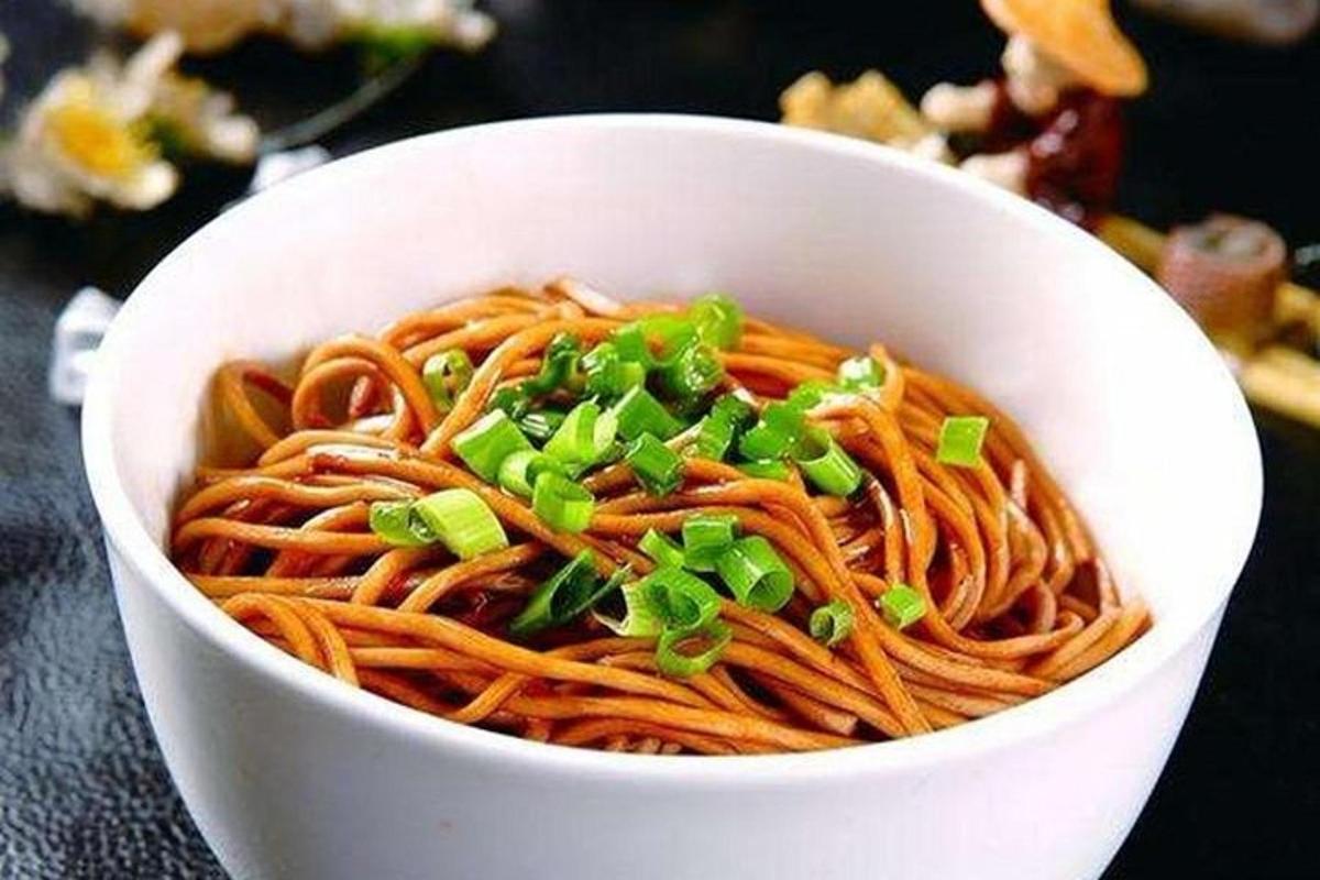 a white bowl of noodles with green onions on it