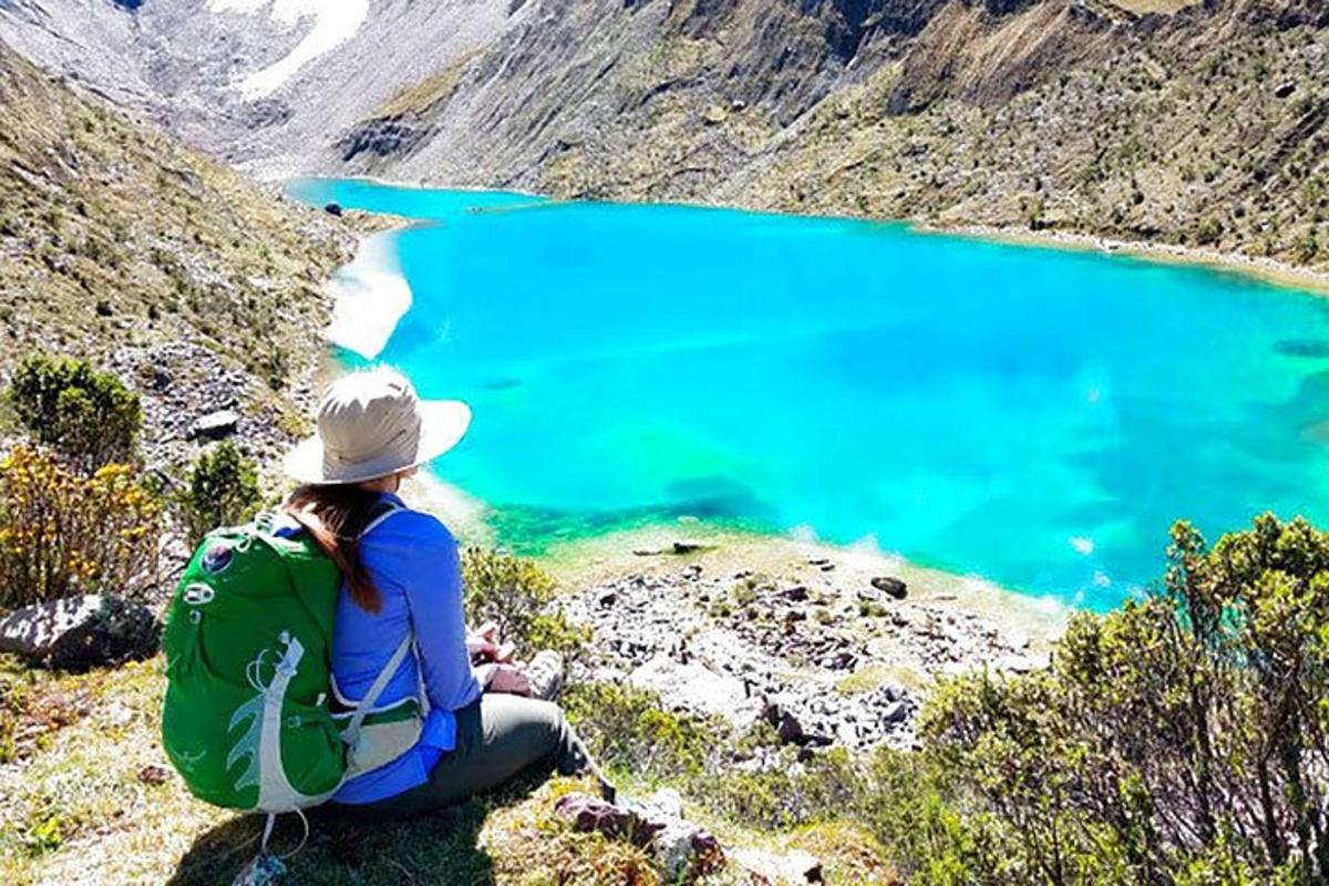 žena s batohem sedící na kopci a dívající se na jezero