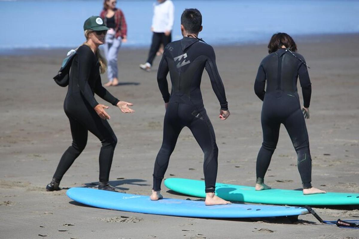 drei Personen in Neoprenanzügen stehen auf Surfbrettern an einem Strand
