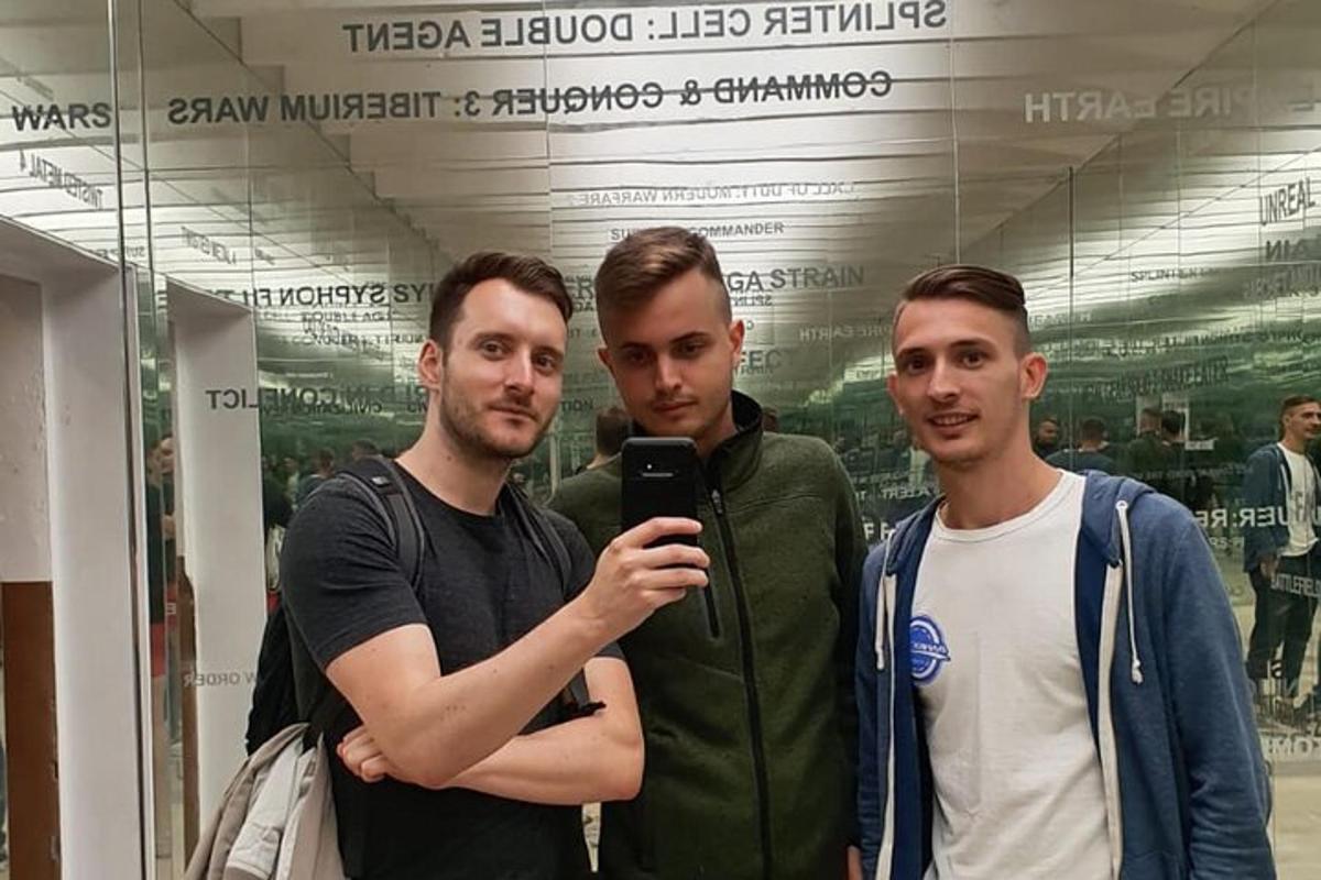 tři muži stojící vedle sebe a dívající se do mobilního telefonu