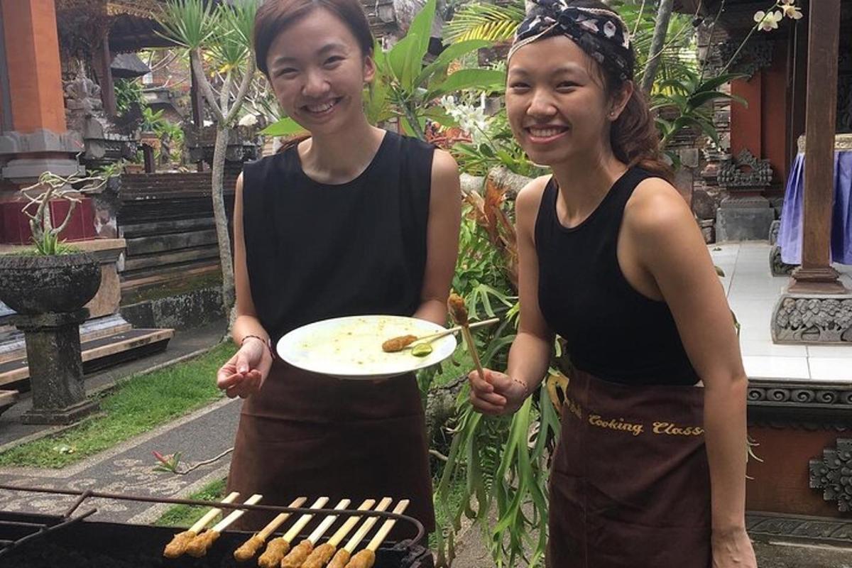 two women holding a plate next to a grill