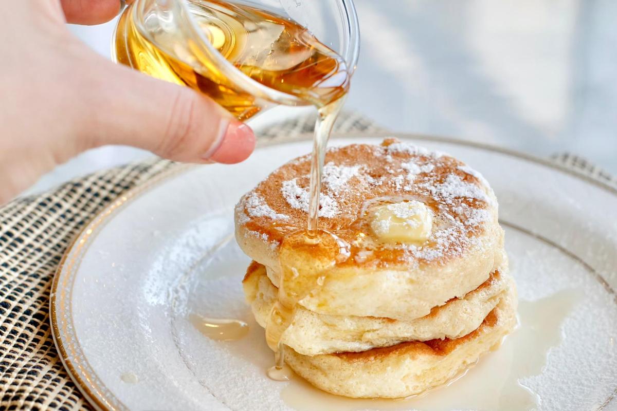 a person is pouring syrup on a stack of pancakes