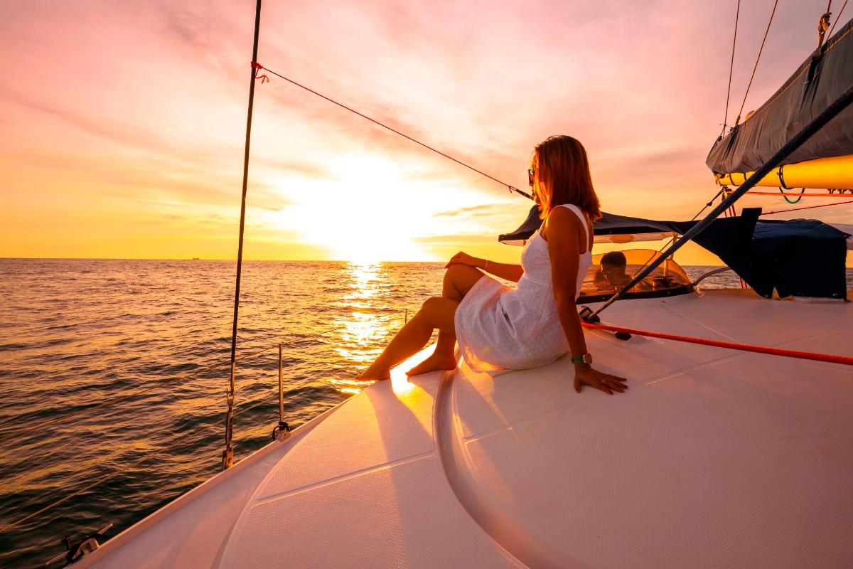 a woman sitting on the bow of a sail boat as the sun sets