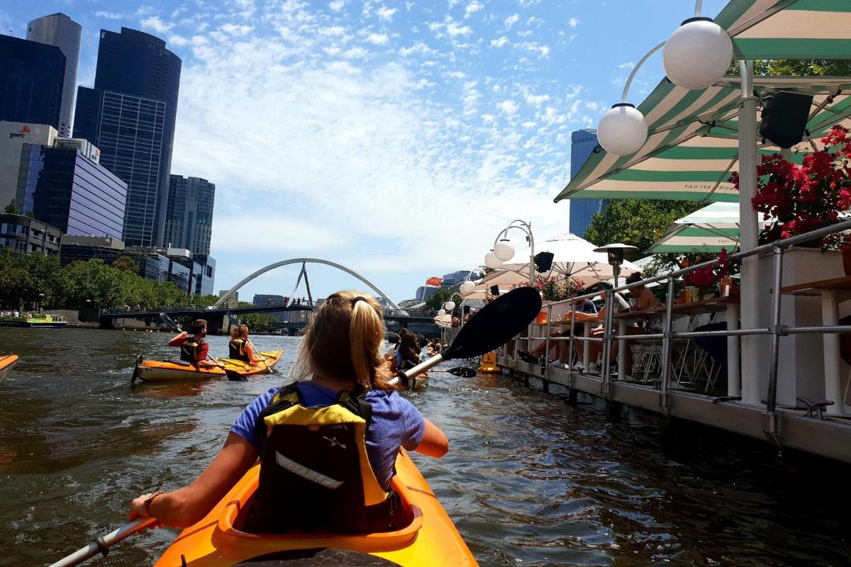 một cô gái trẻ chèo thuyền kayak dọc theo một con sông trong thành phố