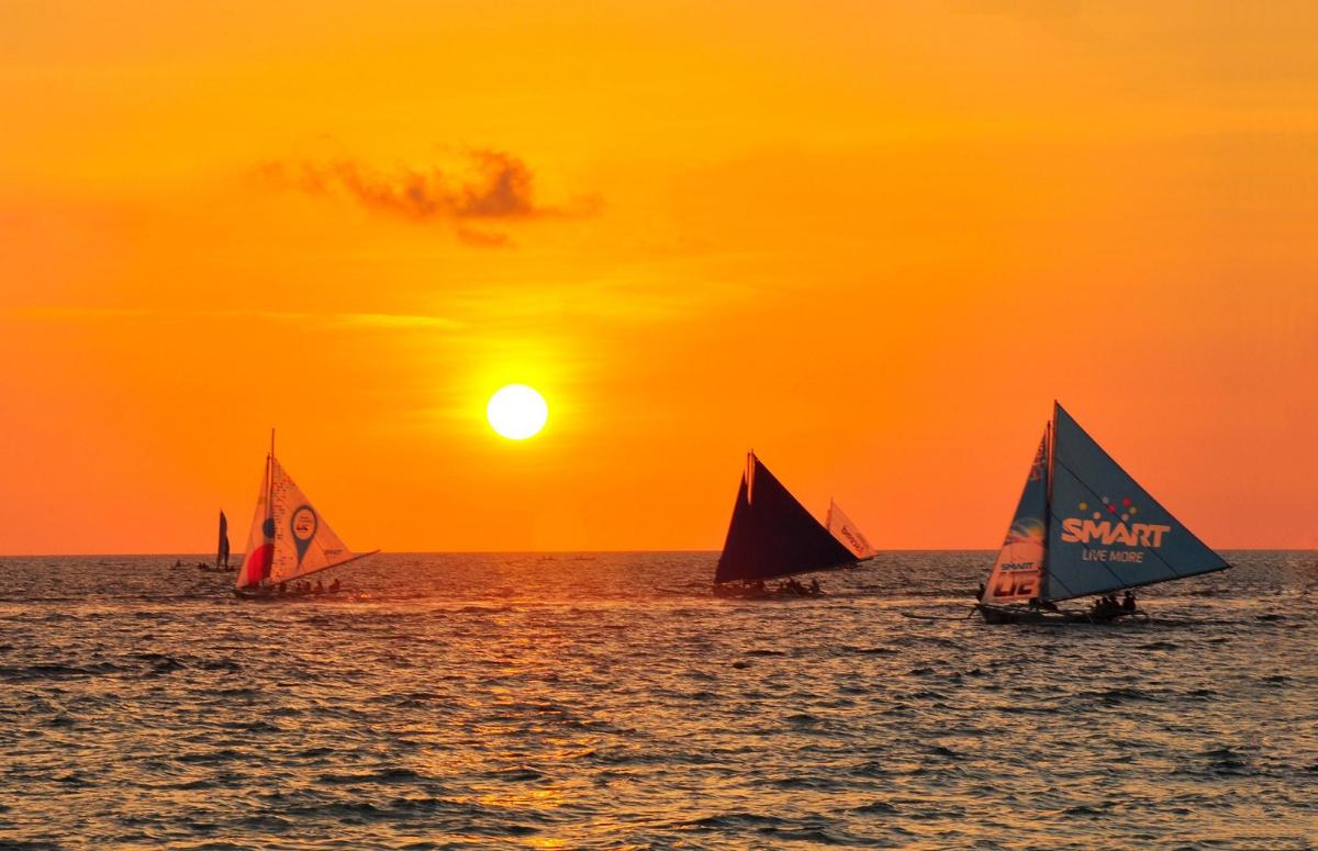 three small sailboats in the ocean at sunset