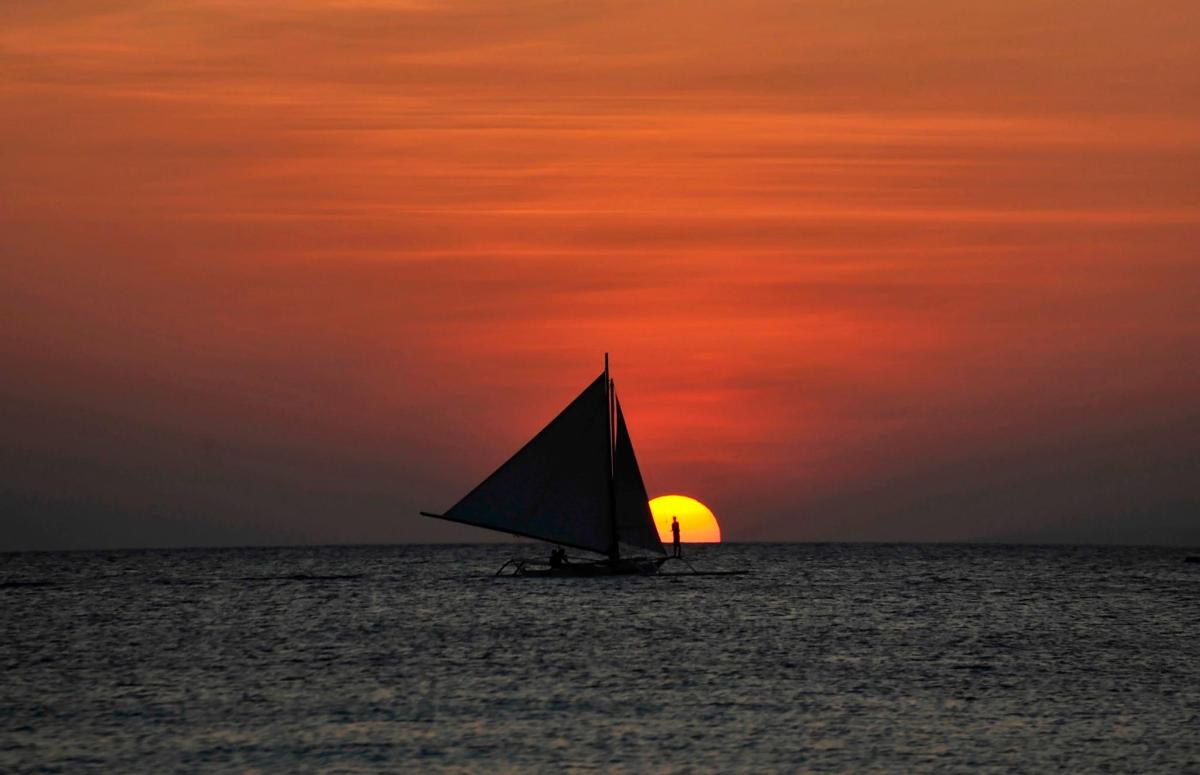 a sail boat in the ocean with a sunset