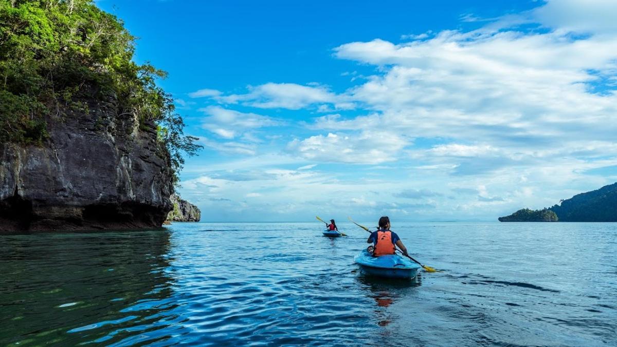 two people in kayaks in the water near a cliff