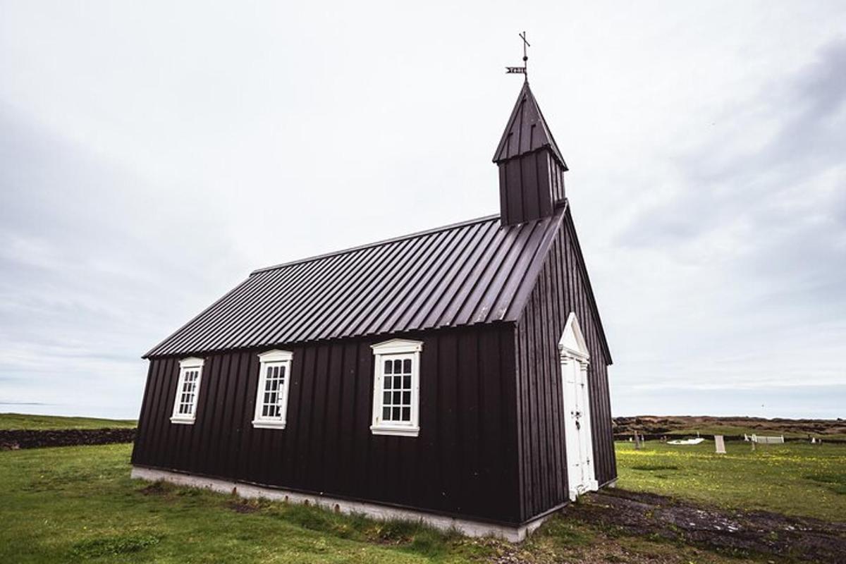 Una iglesia negra con un campanario en un campo de hierba
