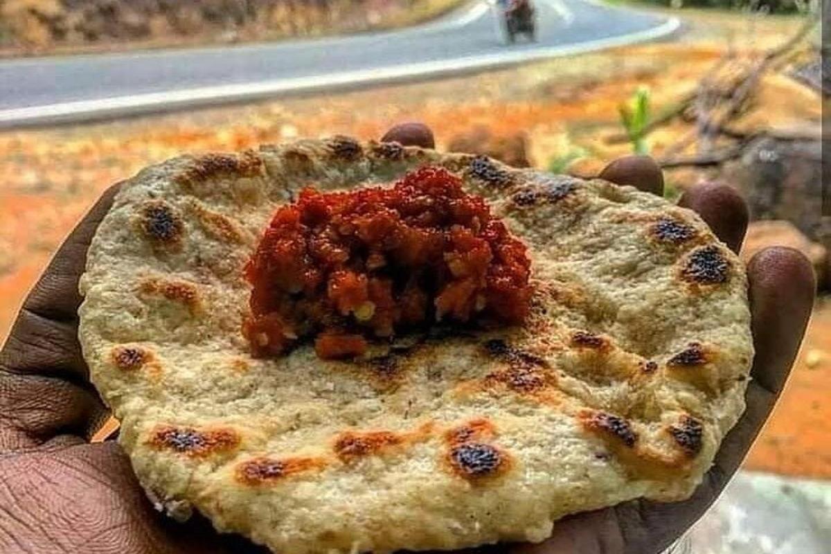 a hand holding a pizza with sauce on it