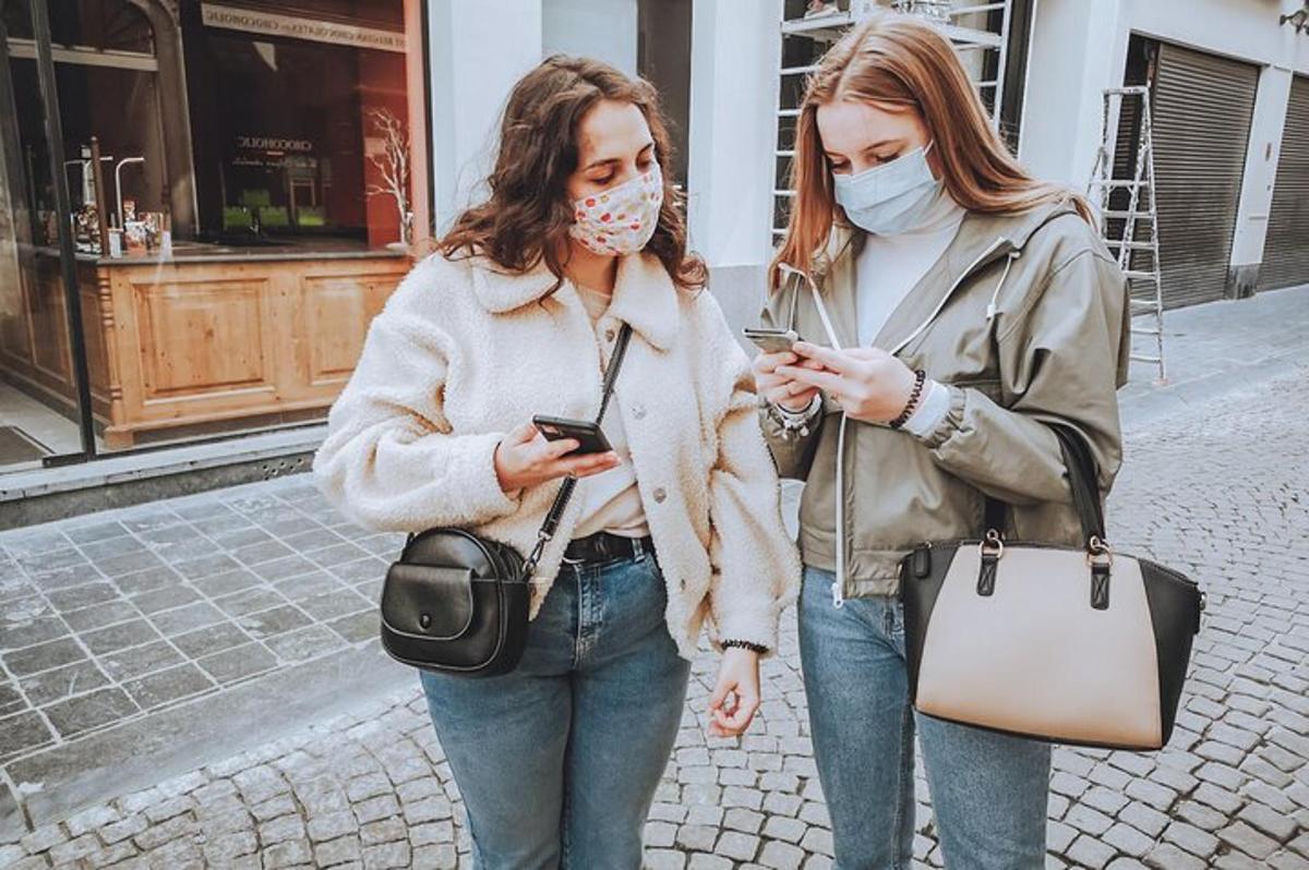 Dvě ženy v rouškách jdou po ulici a dívají se do svých mobilních telefonů