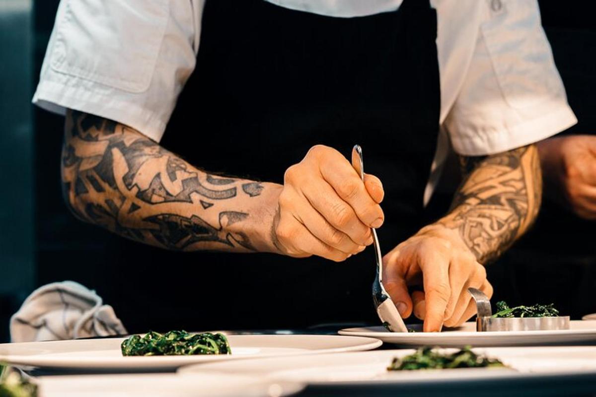 un home amb tatuatges als braços preparant menjar en un plat