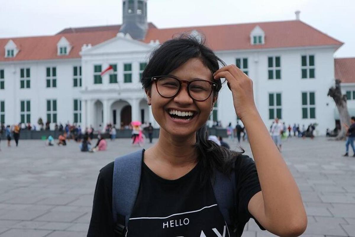 a woman wearing glasses standing in front of a building
