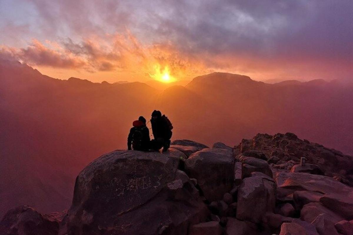 Dos personas sentadas en la cima de una montaña al atardecer