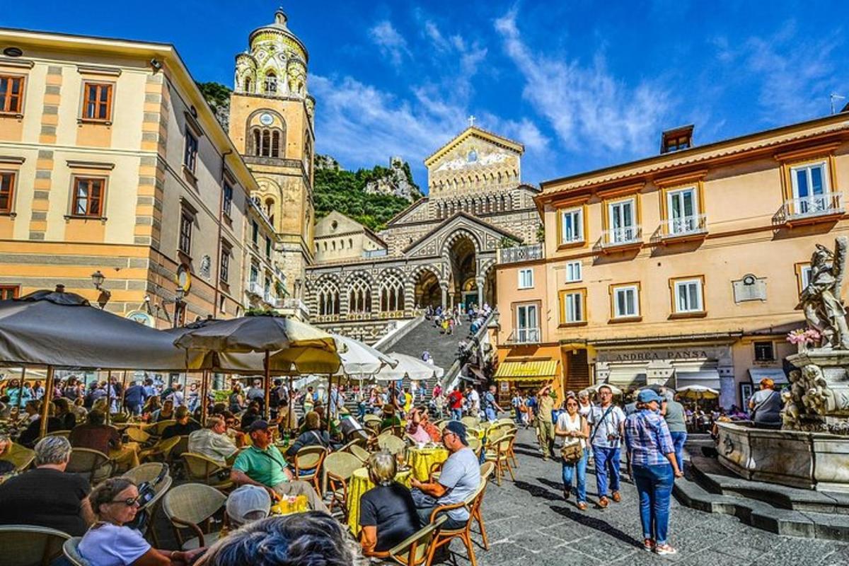 un gruppo di persone sedute ai tavoli in una strada con una torre dell'orologio