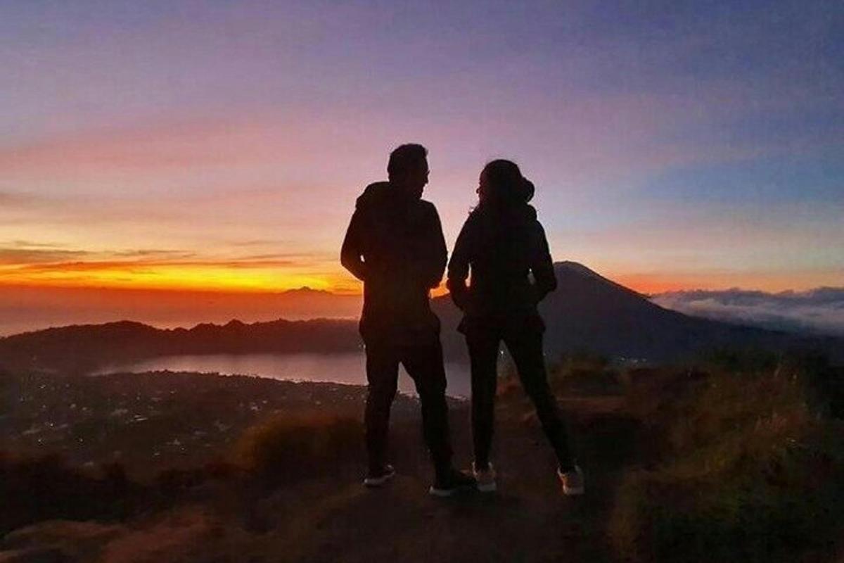 a couple standing on top of a mountain at sunset