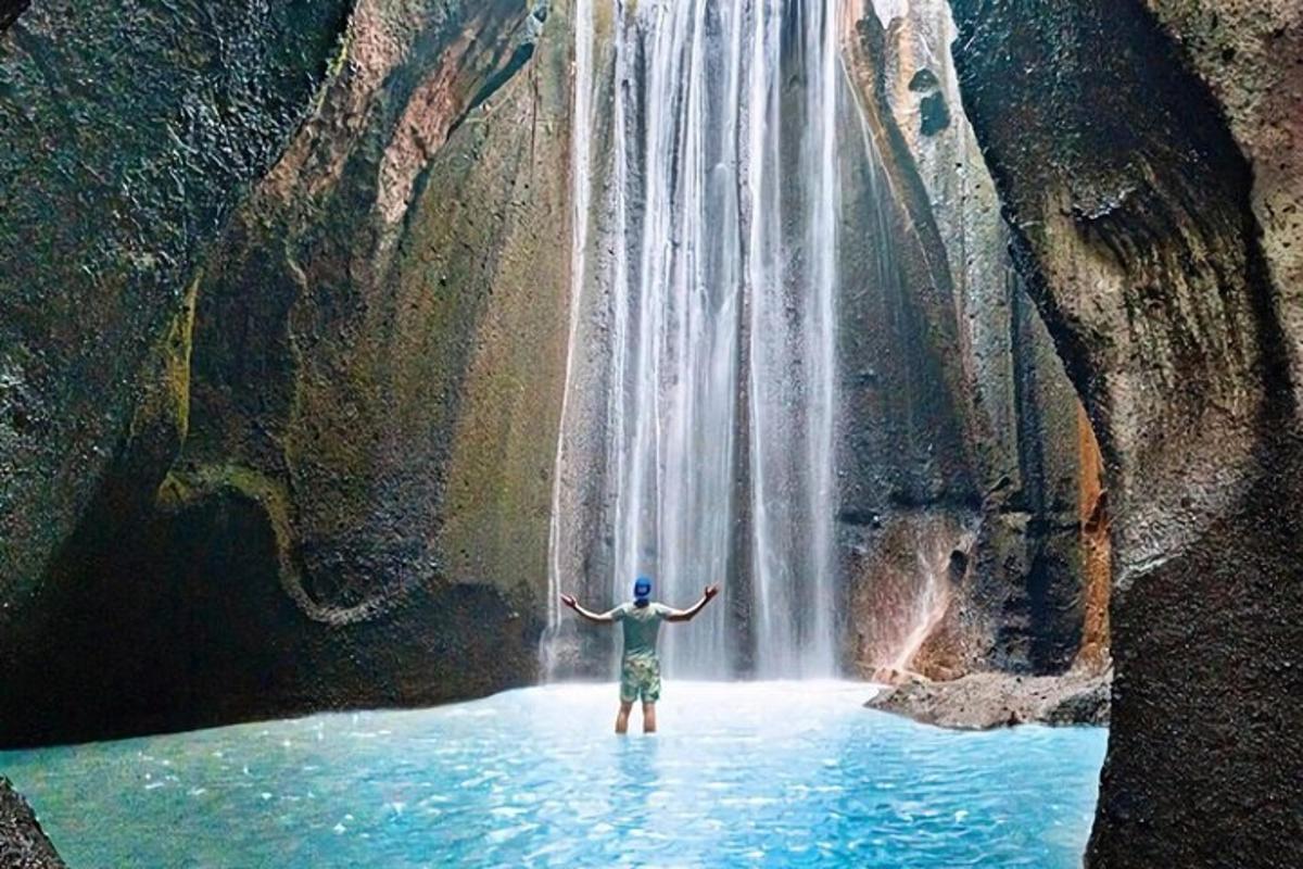 Ένας άντρας στέκεται στο νερό μπροστά σε έναν καταρράκτη