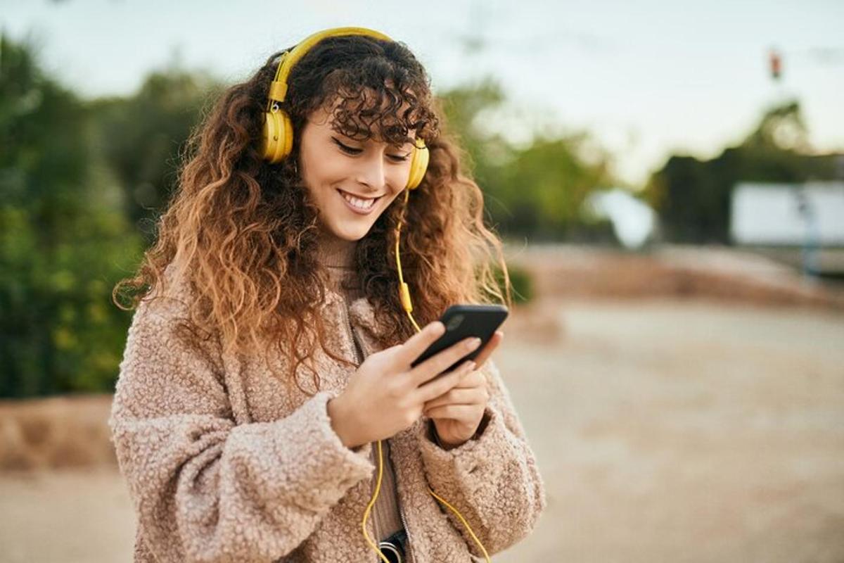 kulaklık takan ve cep telefonuna bakan genç bir kadın