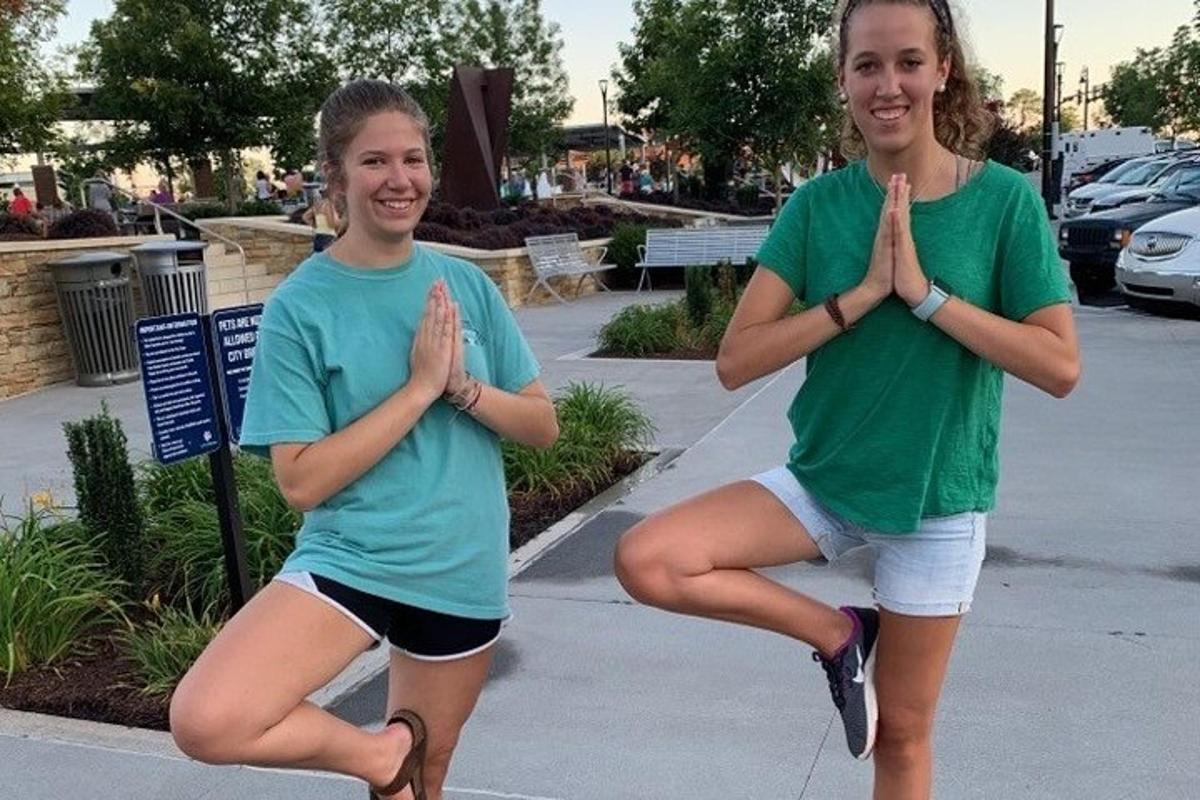 Dos chicas están haciendo yoga en un estacionamiento.