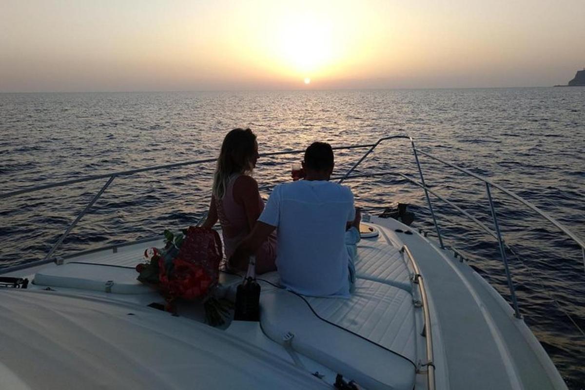 un home i una dona asseguts en un vaixell mirant la posta de sol