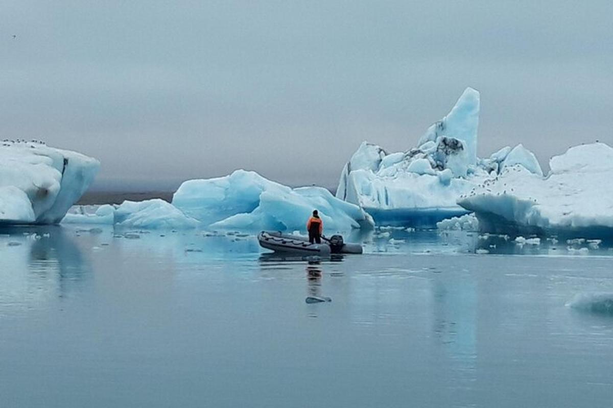 Maður í bát í vatninu við hliðina á ísjökum