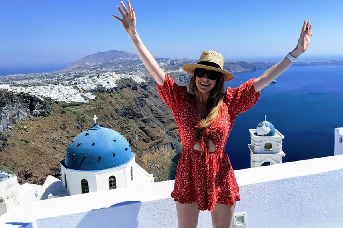 una donna con un vestito rosso e un cappello in piedi su una sporgenza con le braccia alzate