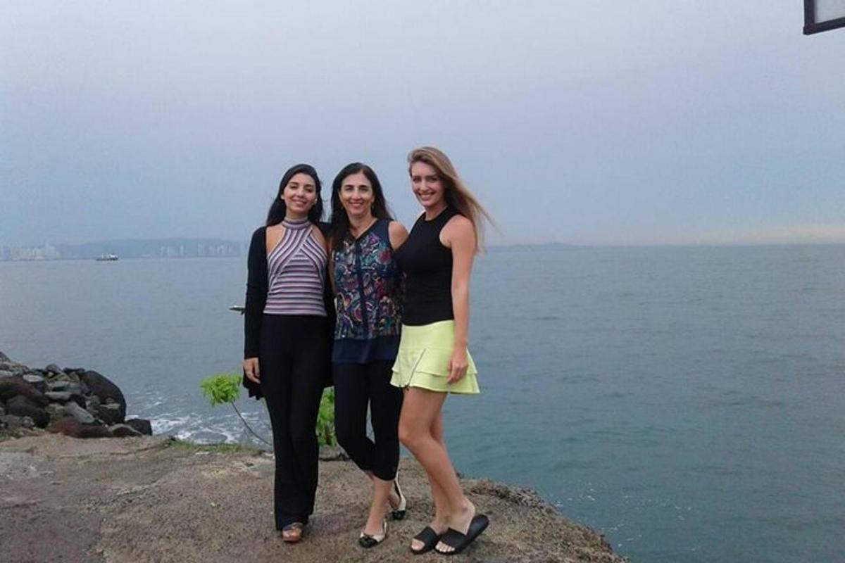 três mulheres em pé sobre uma rocha perto da água
