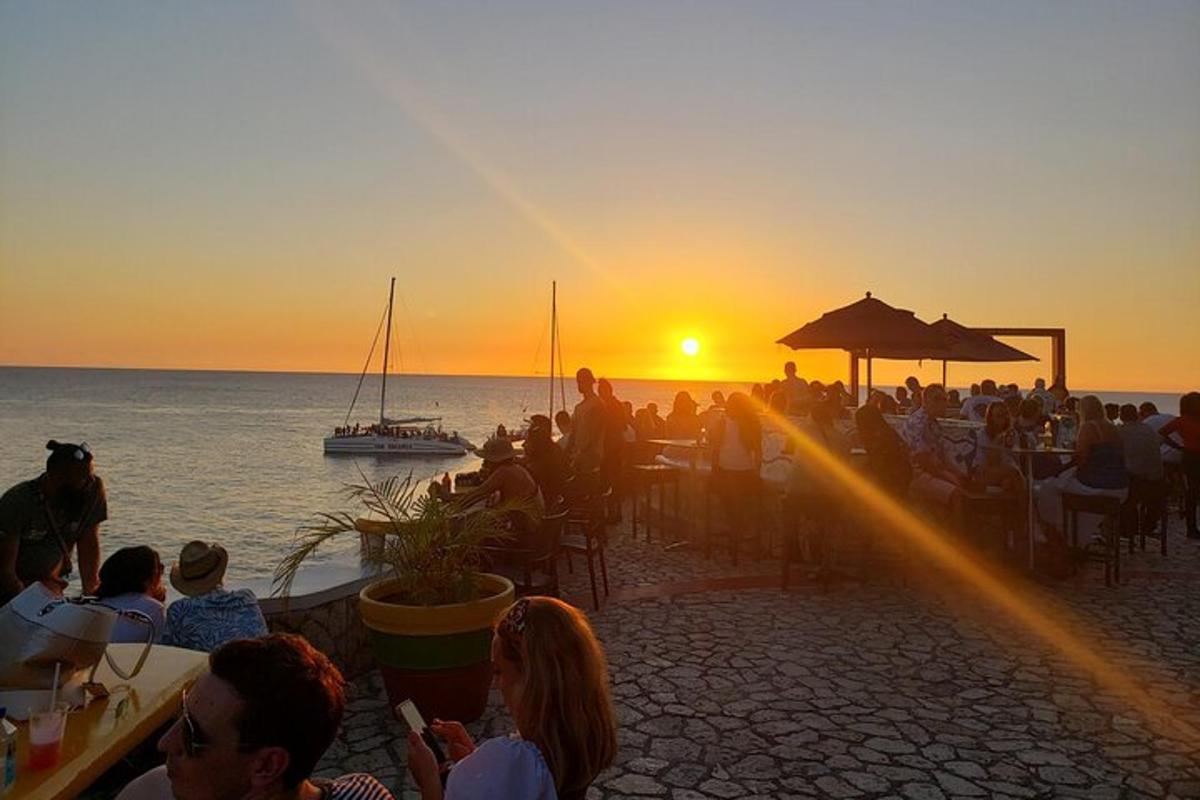 um grupo de pessoas sentadas em mesas assistindo ao pôr do sol