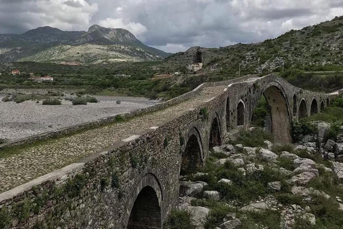 uma ponte de pedra sobre um rio com montanhas ao fundo