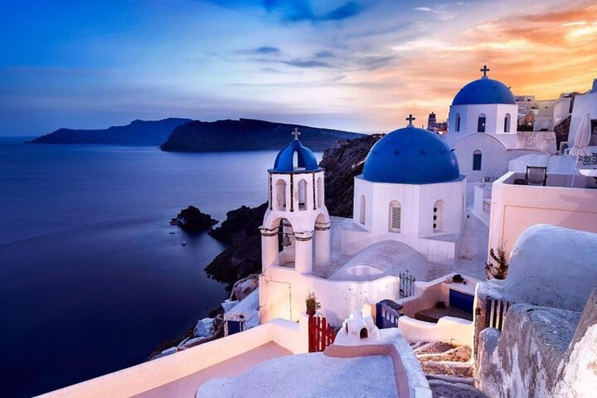 a group of white buildings with blue domes and the ocean