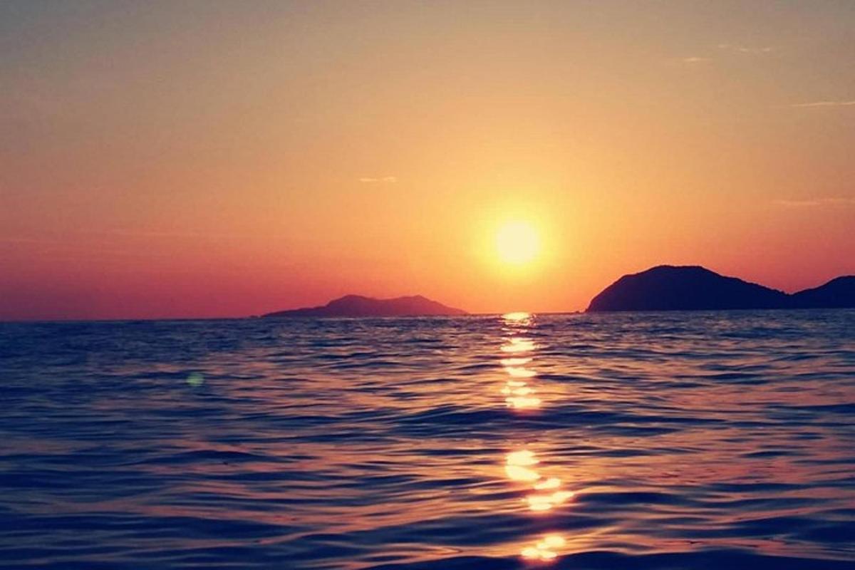 Ηλιοβασίλεμα πάνω από τον ωκεανό με βουνά στο φόντο