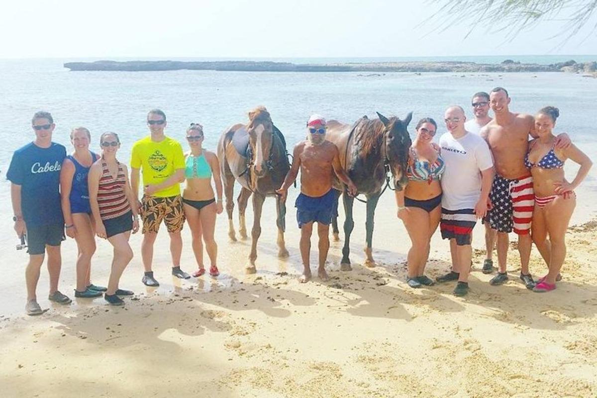 un gruppo di persone in piedi sulla spiaggia con i cavalli