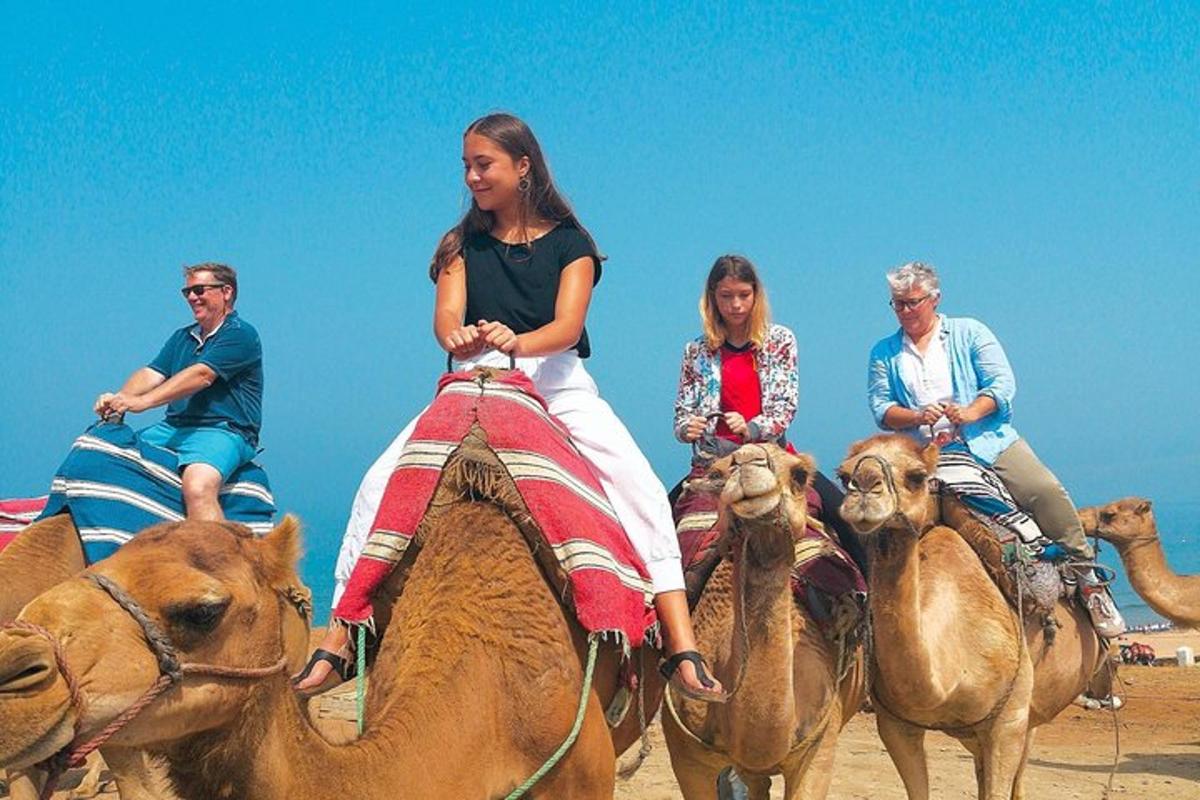 skupina lidí jedoucích na velbloudech na pláži