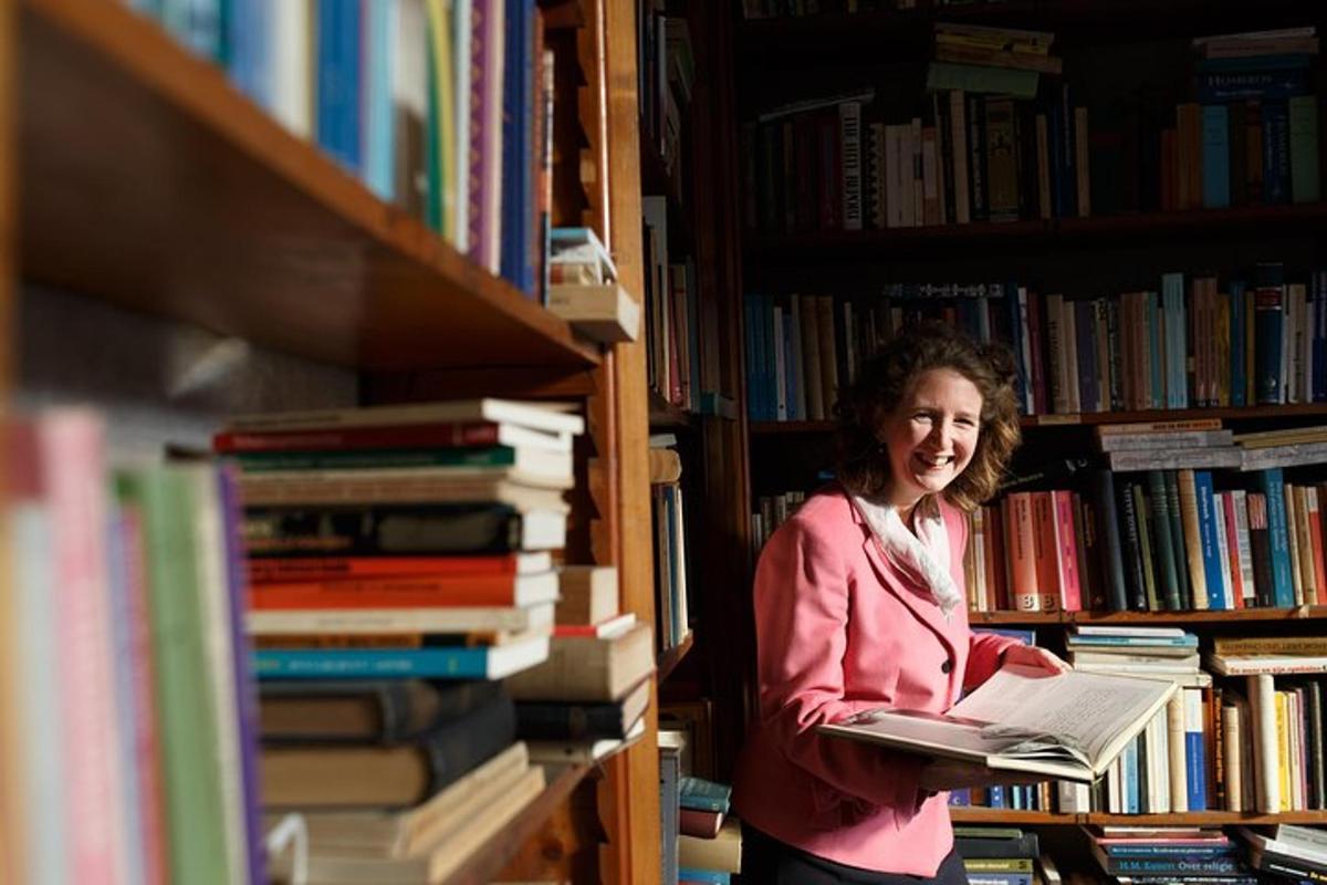 Una mujer parada en una biblioteca sosteniendo un libro.