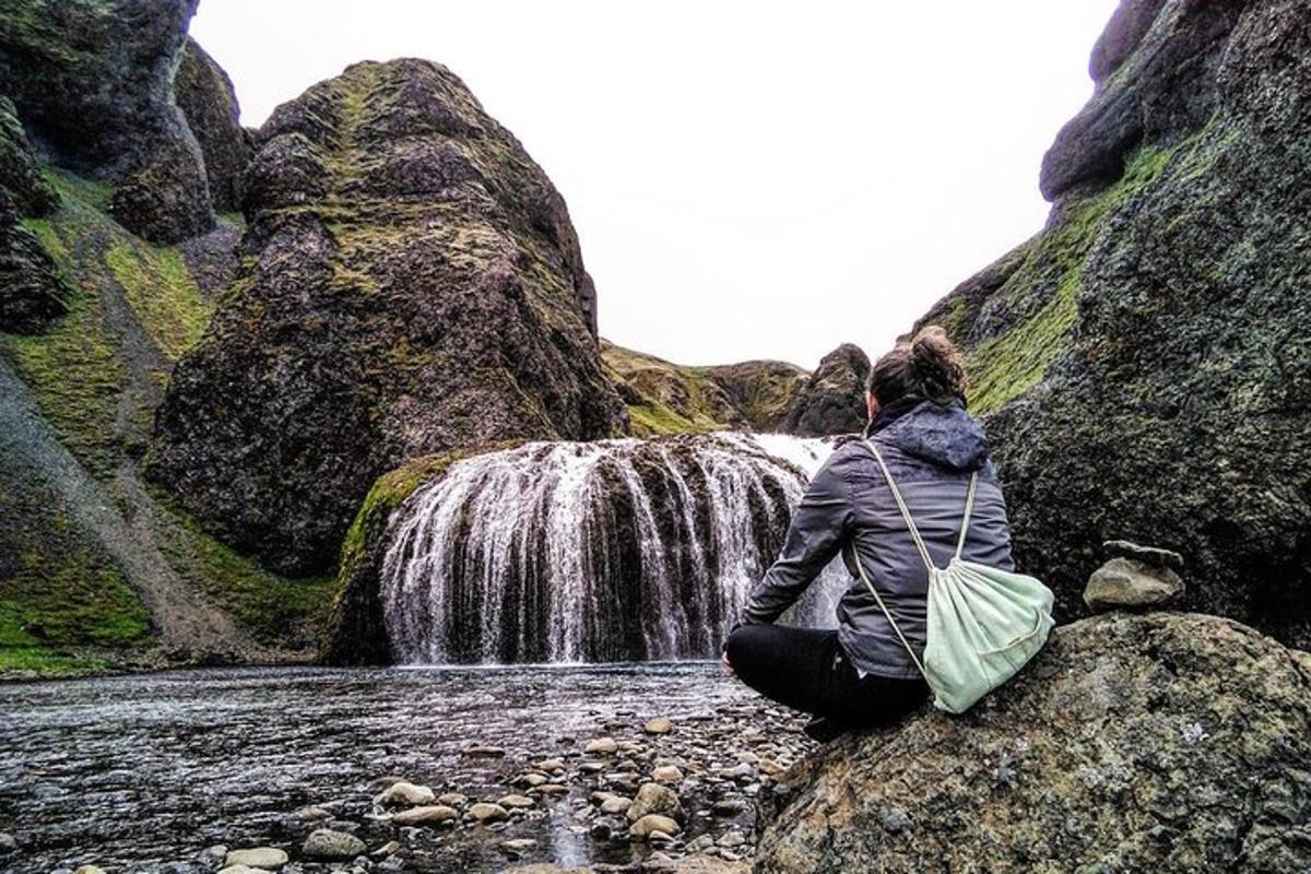seorang wanita duduk di atas batu di depan air terjun