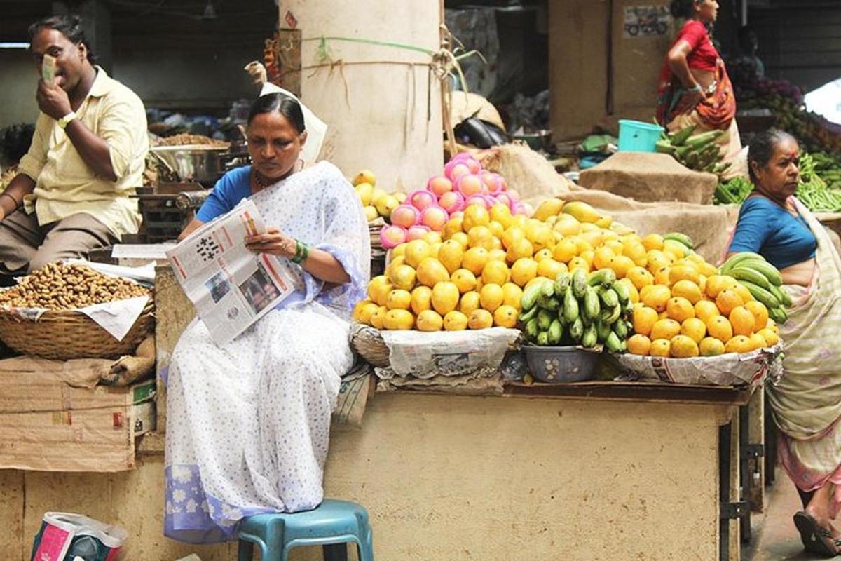 una donna seduta su uno sgabello davanti a una bancarella di frutta