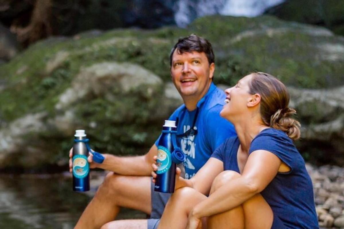 un uomo e una donna seduti accanto a un fiume con in mano delle bottiglie d'acqua