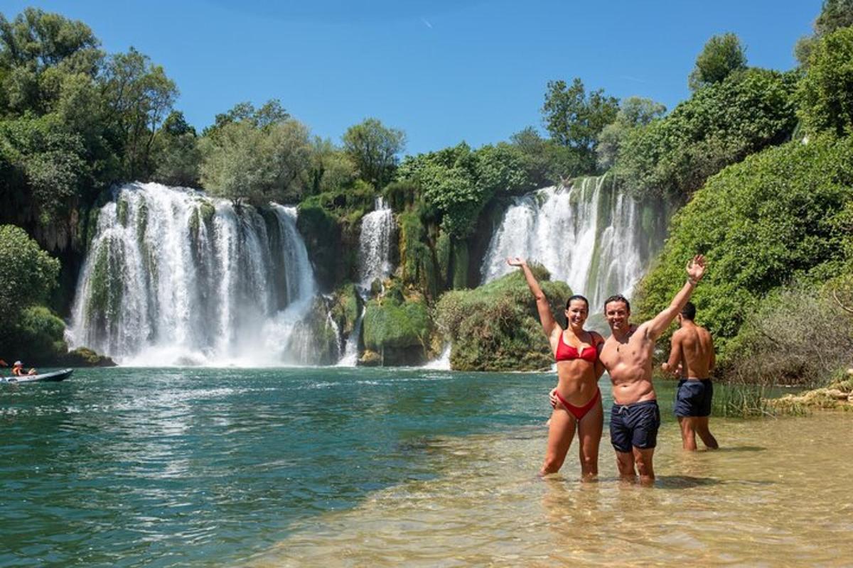 tre persone in piedi nell'acqua di fronte a una cascata