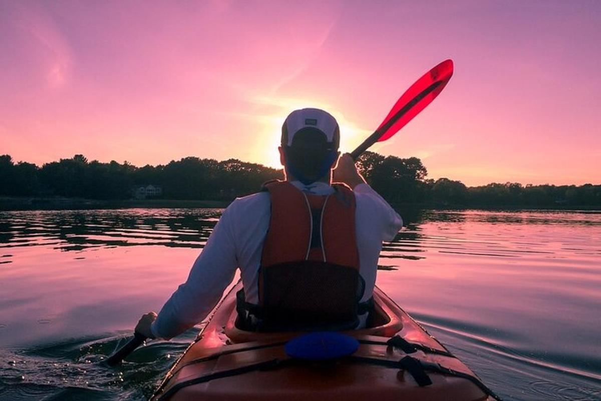 seorang pria di kayak di atas air saat matahari terbenam