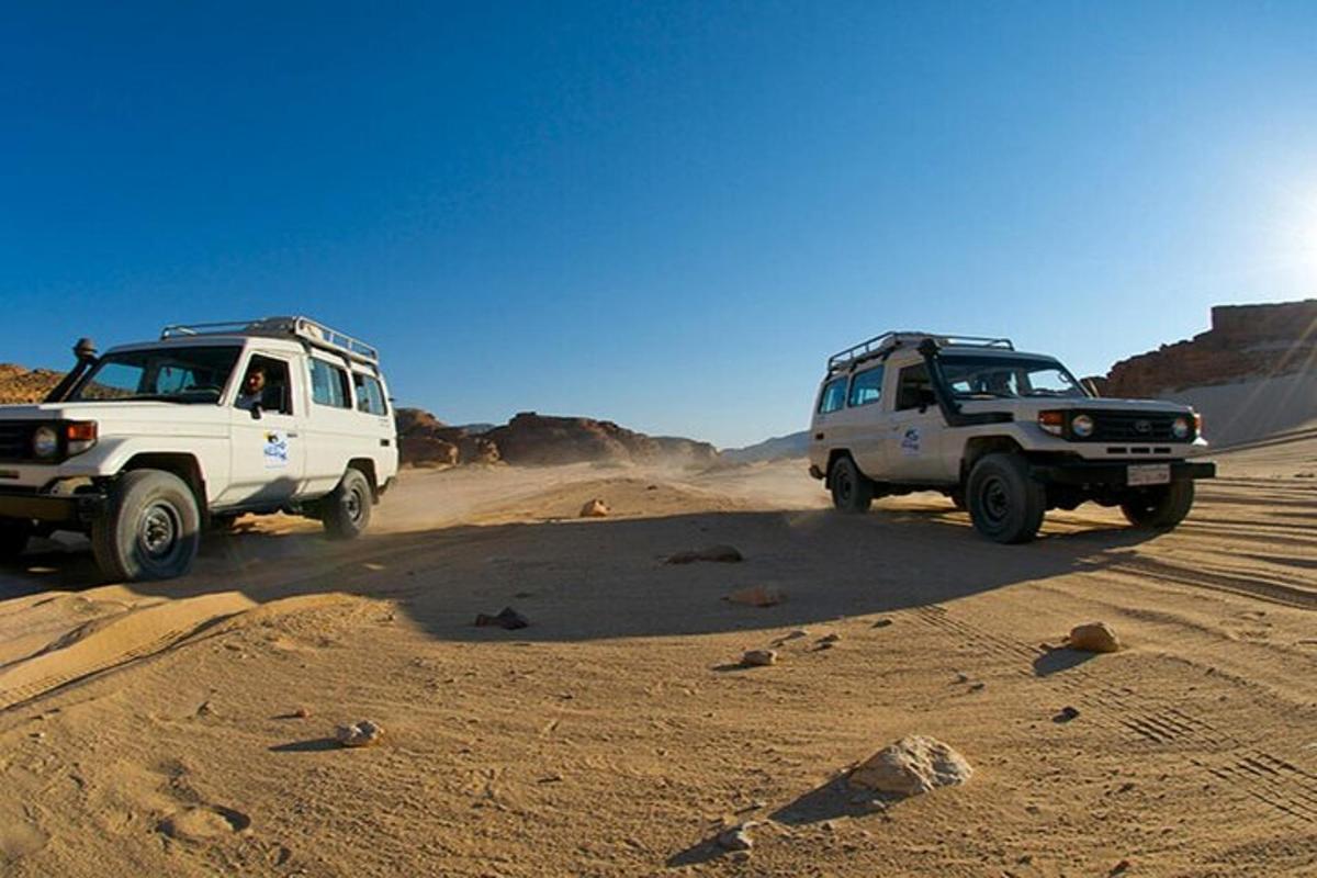 two trucks driving on a dirt road in the desert