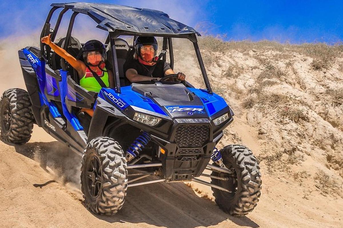 土の上を青いATVに乗って走る二人