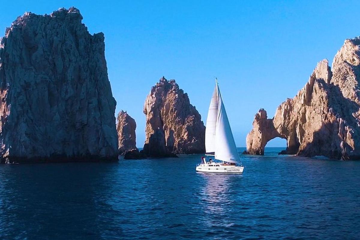 una barca con una vela bianca in acqua vicino alle rocce