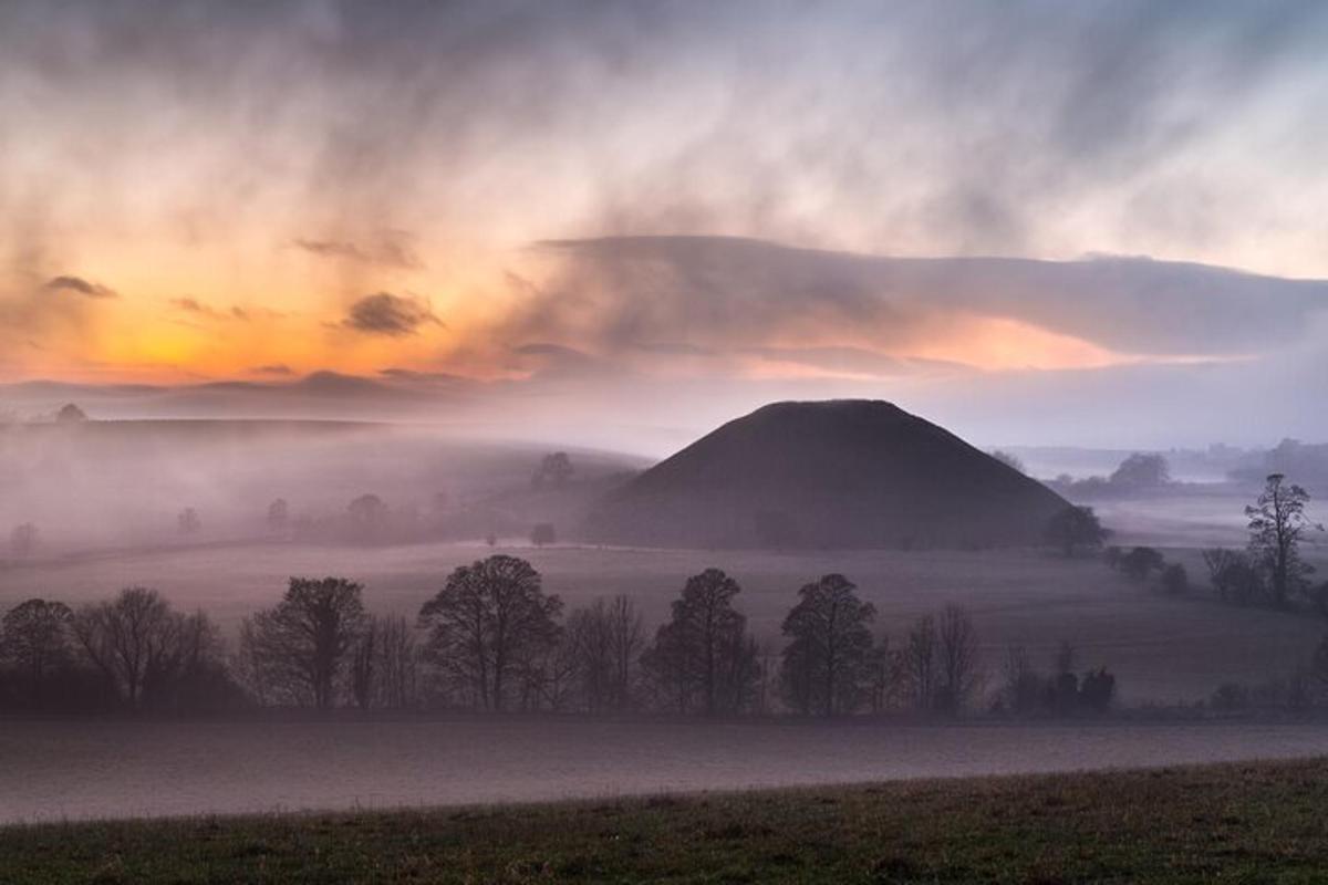 Un campo brumoso con una colina al fondo con una puesta de sol