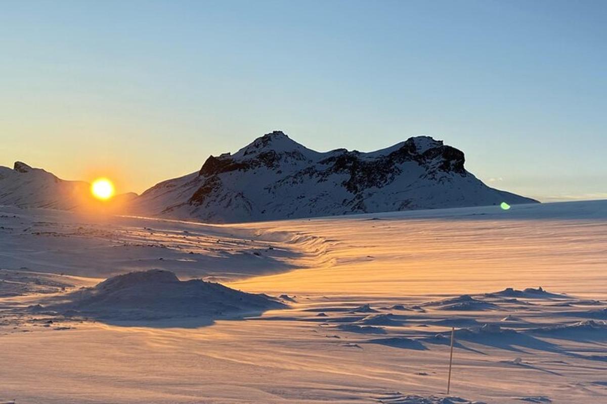 ein Sonnenuntergang über einem schneebedeckten Feld mit einem Berg