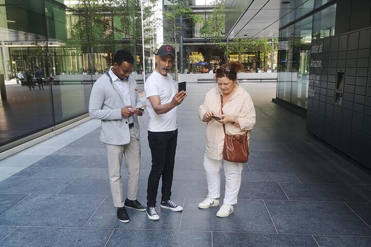 trije ljudje stojijo v stavbi in gledajo v svoje mobilne telefone