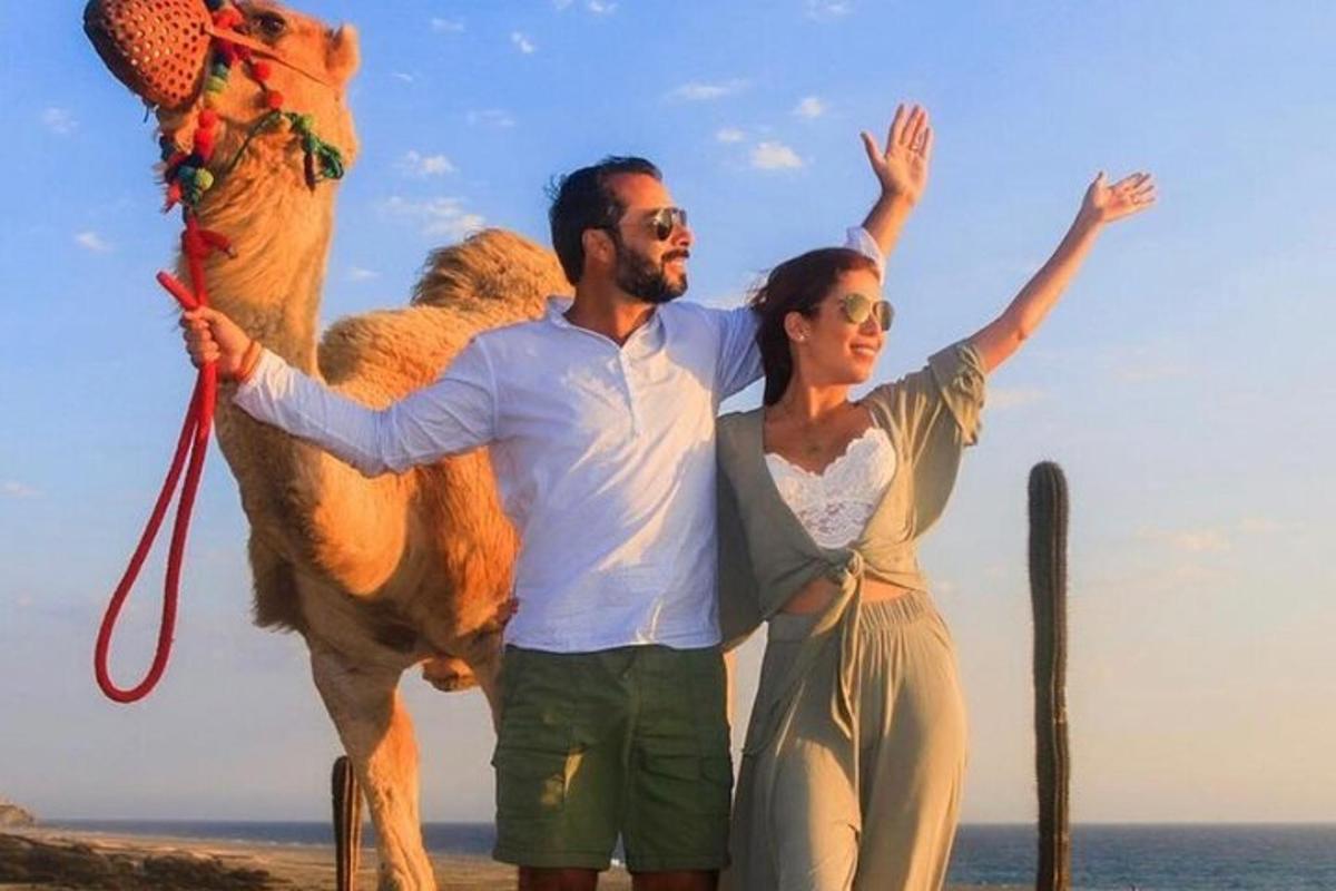 un homme et une femme debout à côté d'un chameau sur la plage