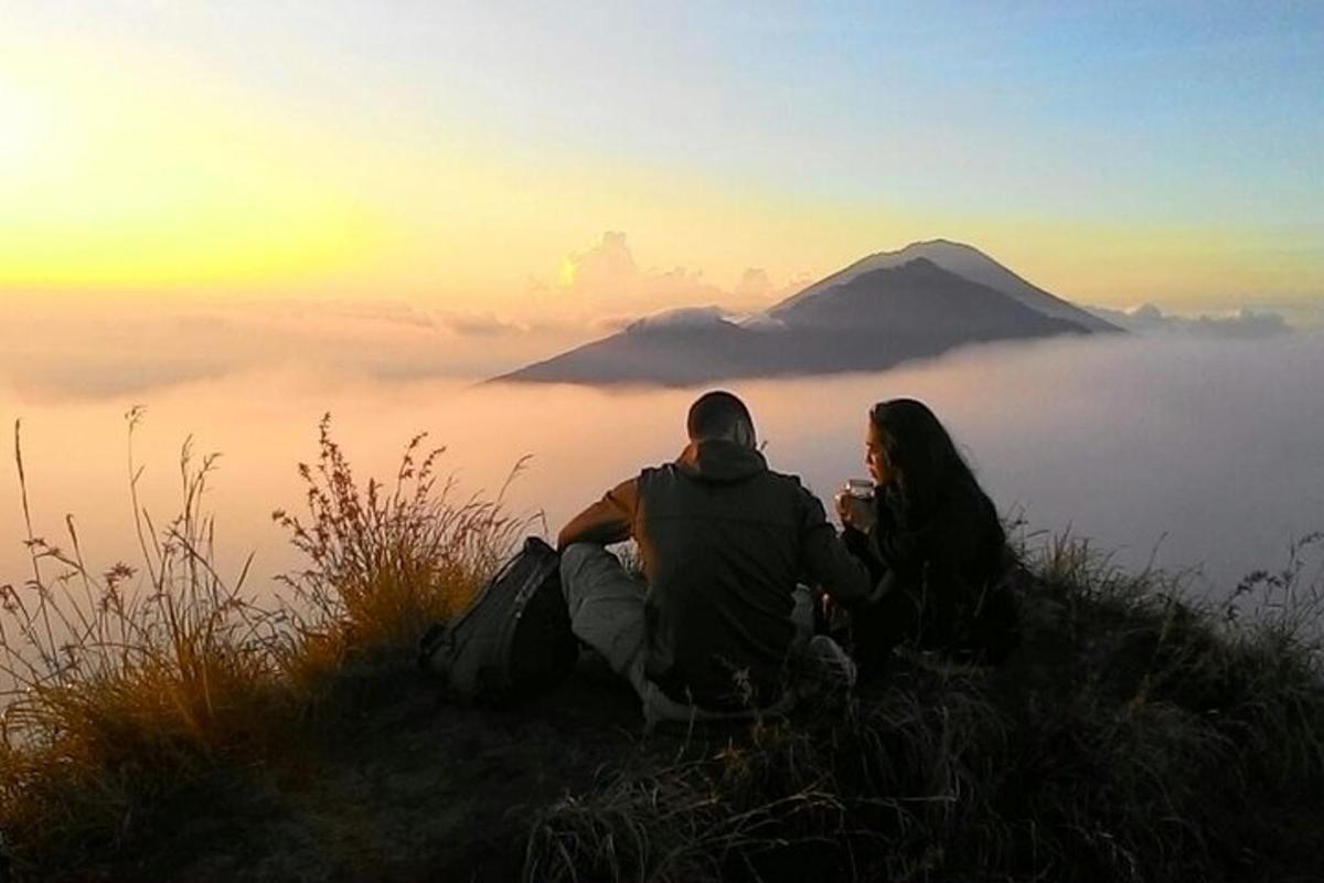 um homem e uma mulher sentados no topo de uma colina com vista para uma montanha coberta de neblina