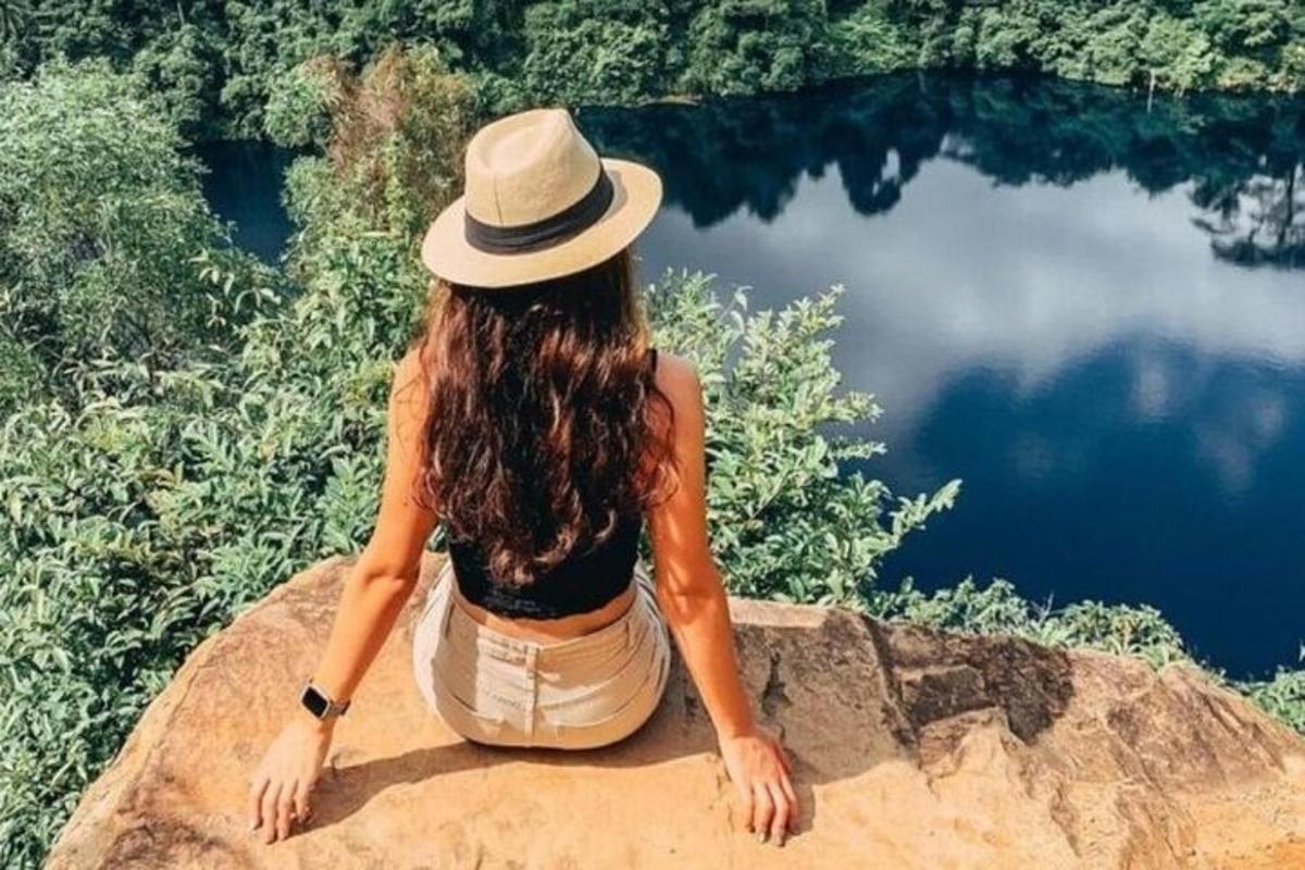 žena v klobouku sedící na skále u jezera