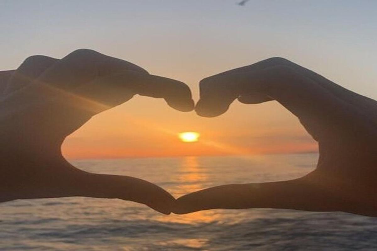 a pair of hands making a heart shape while the sun sets